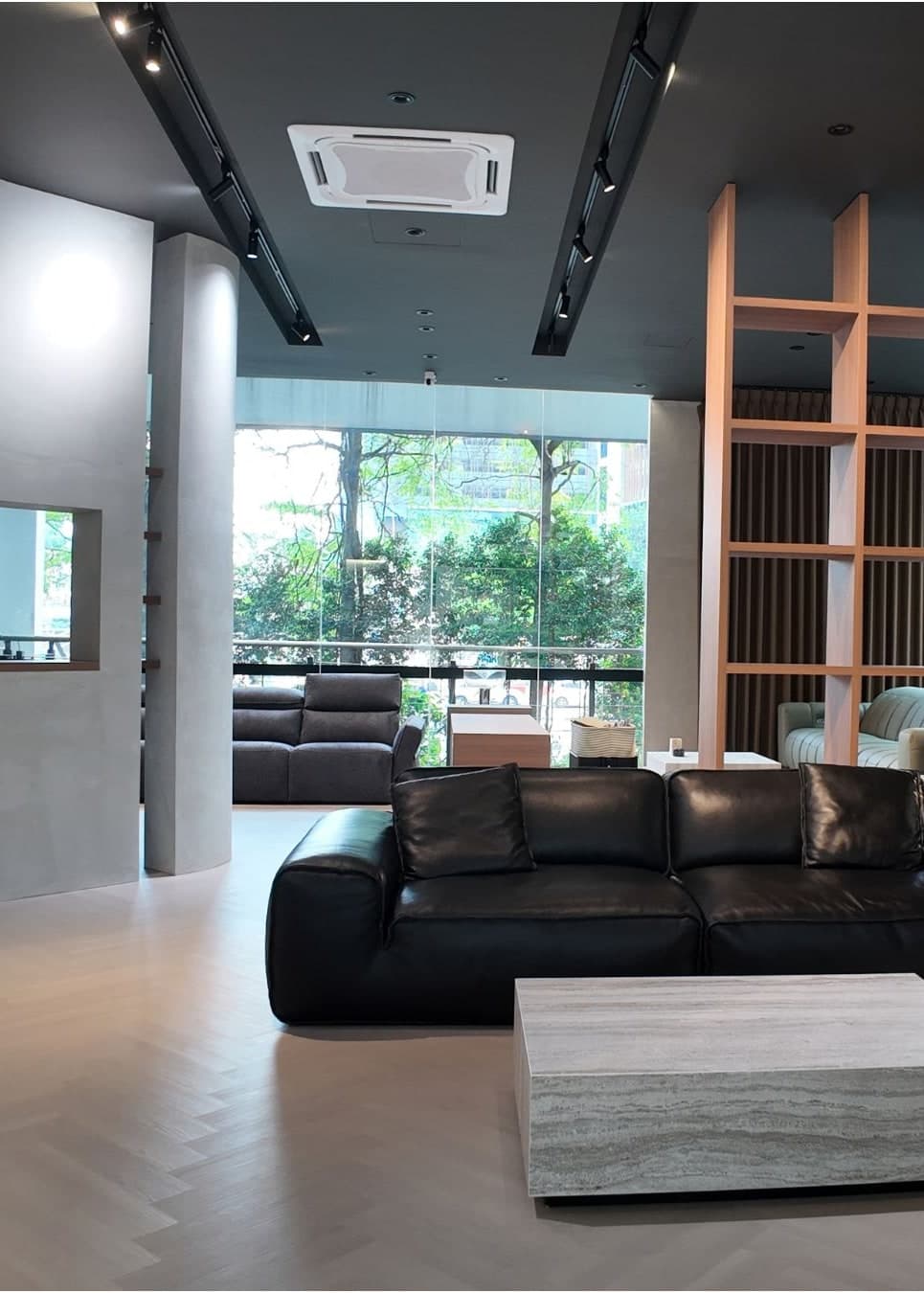 Bangsar showroom lounge with a black leather sofa and full-height windows onto the trees