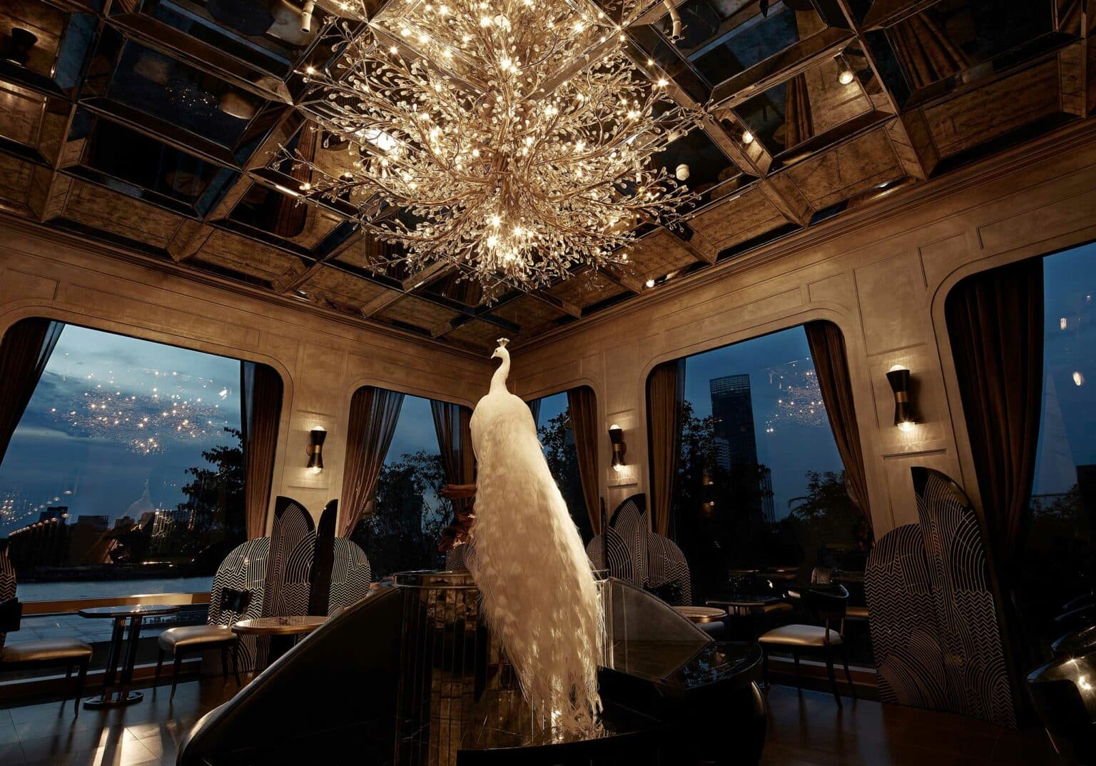Evening cocktail salon with a tree-like crystal chandelier and bespoke lounge seating by tall windows
