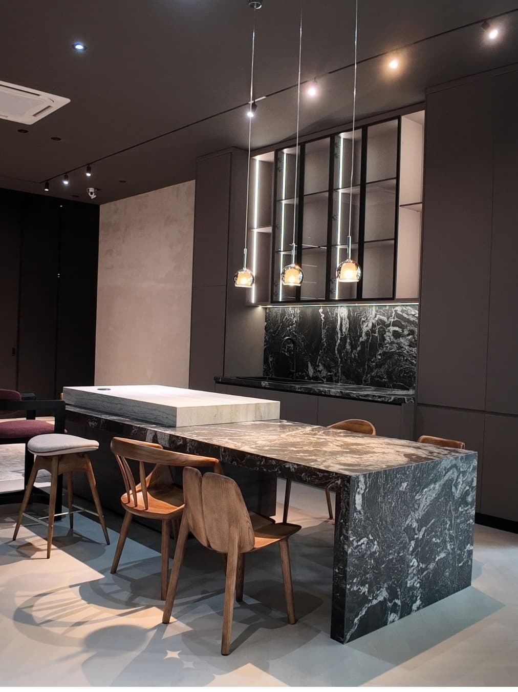 Black marble kitchen island and dining table with timber chairs under glass pendants