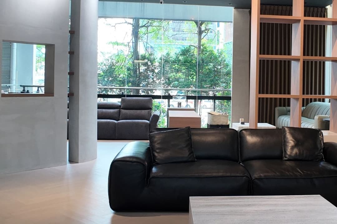 Bangsar showroom lounge with a black leather sofa and full-height windows onto the trees